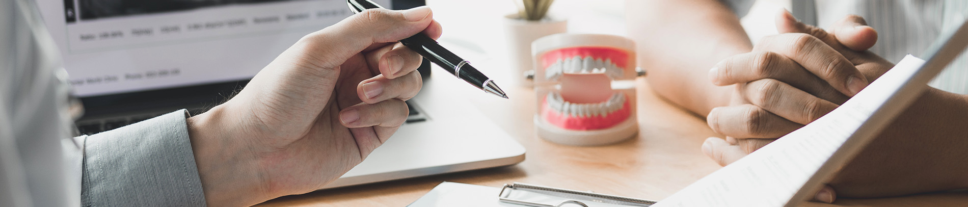 The image shows a group of people, possibly professionals given their attire and the setting that appears to be an office or professional environment. They are gathered around a table with a laptop on it, engaged in what seems to be a discussion or meeting.